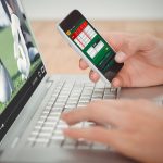 View of lecture app against man holding mobile phone while typing on laptop at desk